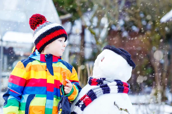 Garoto engraçado em roupas coloridas fazendo um boneco de neve, ao ar livre — Fotografia de Stock