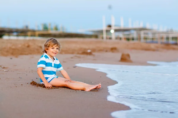 Szczęśliwy chłopiec dziecko zabawy z zamku z piasku przez ocean — Zdjęcie stockowe