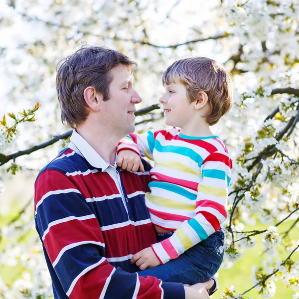 Padre joven y niño pequeño en el jardín floreciente —  Fotos de Stock