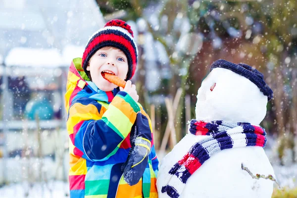 Grappige kind jongen in kleurrijke kleding maken een sneeuwpop, buitenshuis — Stockfoto