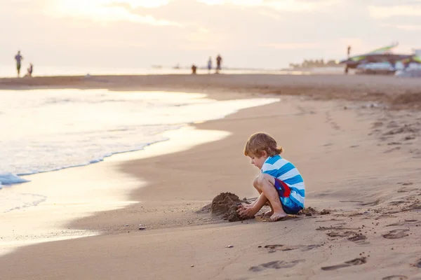 Niño feliz divirtiéndose con arena castillo por océano — Foto de Stock