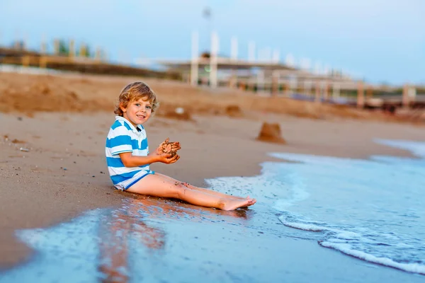 Happy little kid boy having fun with sand castle by ocean — Stock Photo, Image