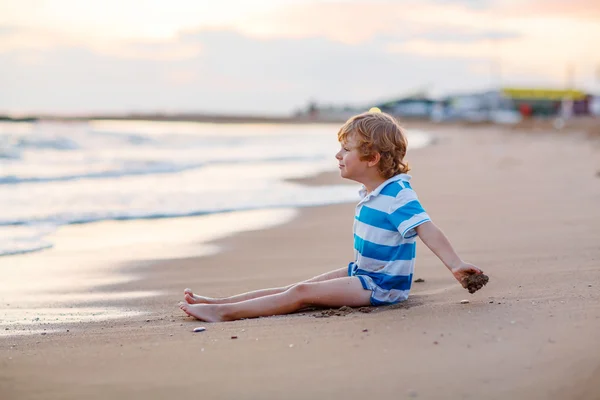 Menino pequeno feliz se divertindo com castelo de areia pelo oceano — Fotografia de Stock