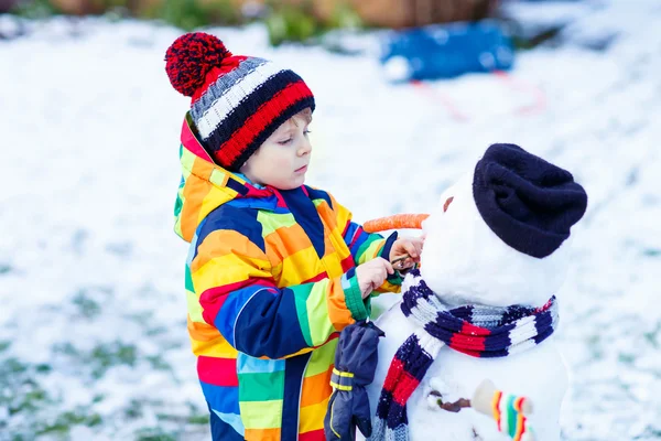 Funny kid boy making a snowman in winter — Stock Photo, Image