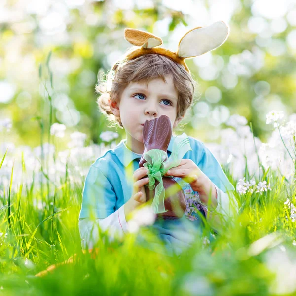 Little toddler wearing Easter bunny ears and eating chocolate at Stock