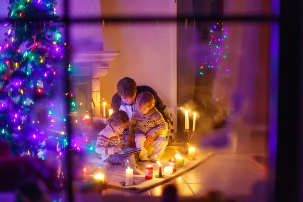 Joven padre y sus pequeños hijos sentados junto a una chimenea en C —  Fotos de Stock