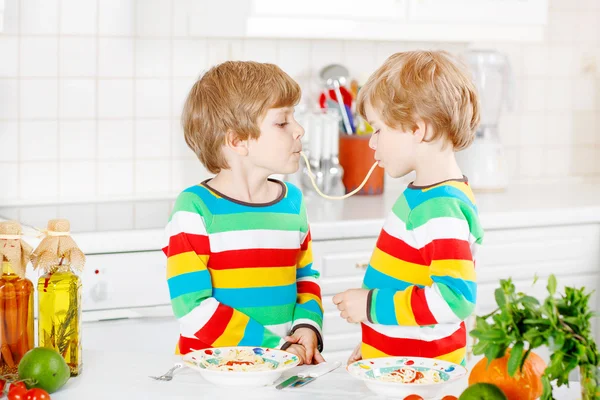 Dos niños comiendo espaguetis en la cocina doméstica . — Foto de Stock