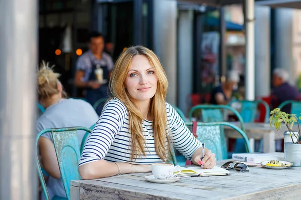 Женщина пьет кофе и пишет заметки в кафе — стоковое фото