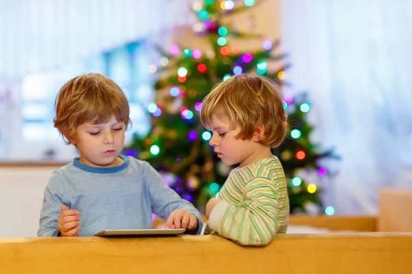 Duas crianças pequenas felizes brincando com tablet pc, dentro de casa — Fotografia de Stock