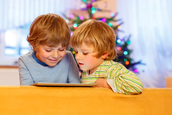 Duas crianças pequenas felizes brincando com tablet pc, dentro de casa — Fotografia de Stock