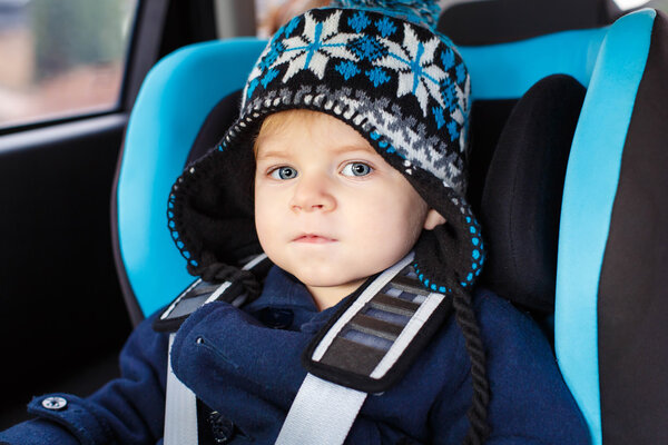 Adorable toddler boy sitting in safety car seat 
