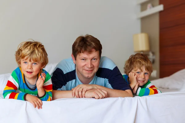 Два маленьких мальчика-брата и папа веселятся в постели после родов — стоковое фото