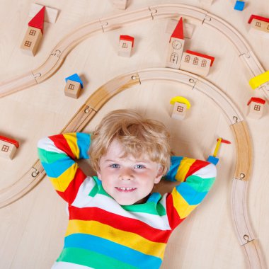 Little blond child playing with wooden railroad trains indoor