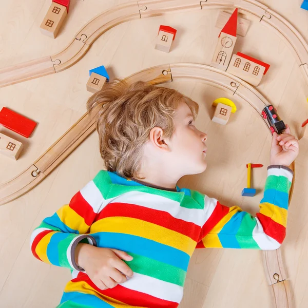 Little blond child playing with wooden railroad trains indoor — Stockfoto