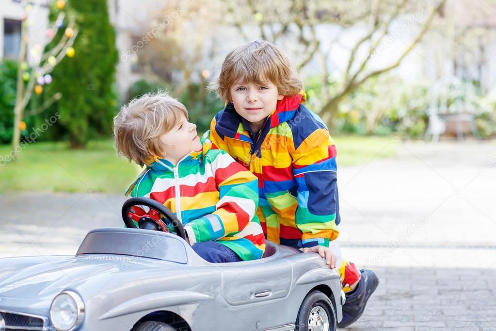 Two happy sibling boys playing with big old toy car