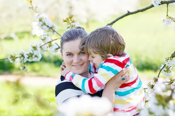Joven madre y niño pequeño divirtiéndose en el jardín floreciente —  Fotos de Stock
