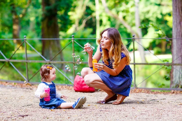 Mãe e menina soprando bolhas de sabão no parque — Fotografia de Stock