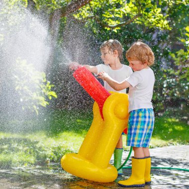 İki küçük çocuk bahçe hortumu ve su ile oynarken yaz aylarında