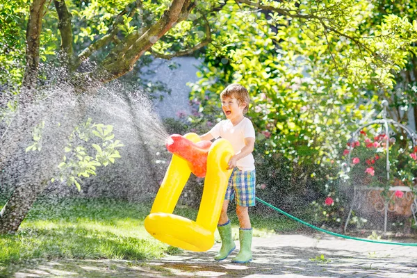 En liten guttunge som leker med en hageslange – stockfoto