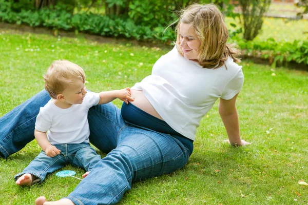 Donna incinta e adorabile piccolo figlio bambino in giardino . — Foto Stock