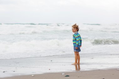 Little kid boy playing on beach on stormy day