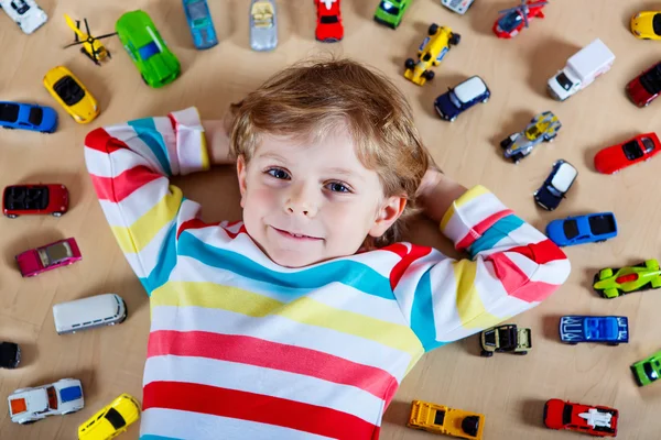 Pequena criança loira brincando com muitos carros de brinquedo interior — Fotografia de Stock