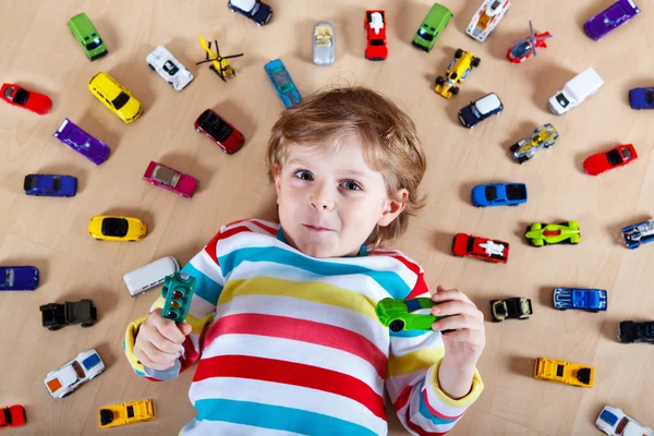 Lilla blonda barn leker med massor av leksaksbilar inomhus — Stockfoto