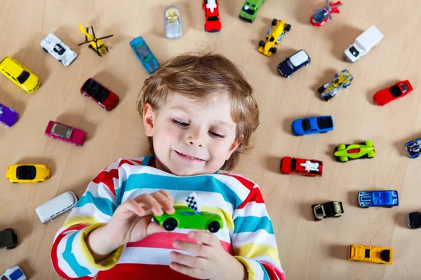 Little blond child playing with lots of toy cars indoor — Stock Photo, Image