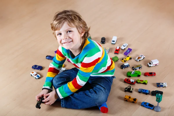 Pequena criança loira brincando com muitos carros de brinquedo interior — Fotografia de Stock