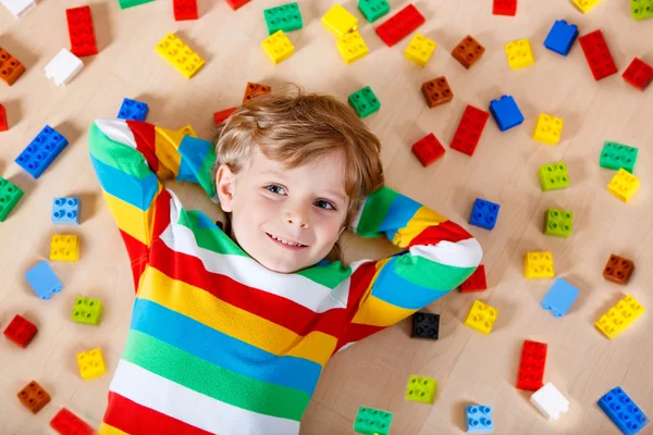 Piccolo bambino biondo che gioca con molti blocchi di plastica colorati — Foto Stock