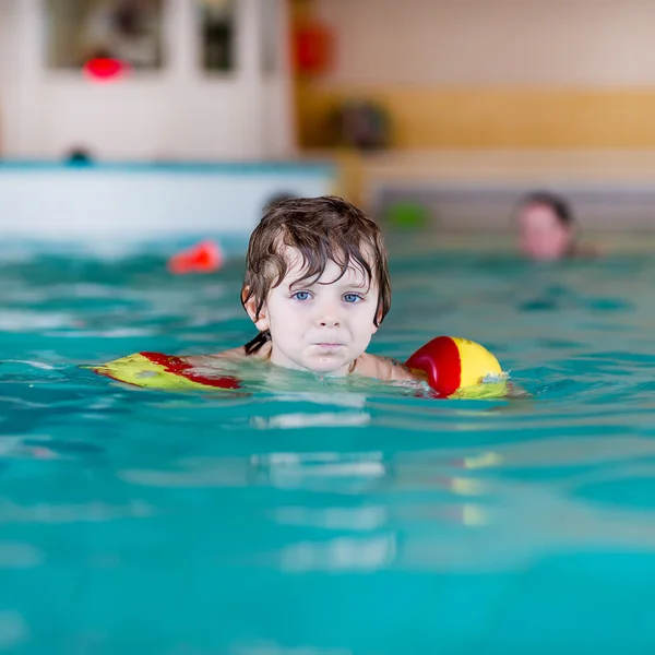 Mały chłopiec dziecko z swimmies uczyć się pływać w krytym basenem — Zdjęcie stockowe