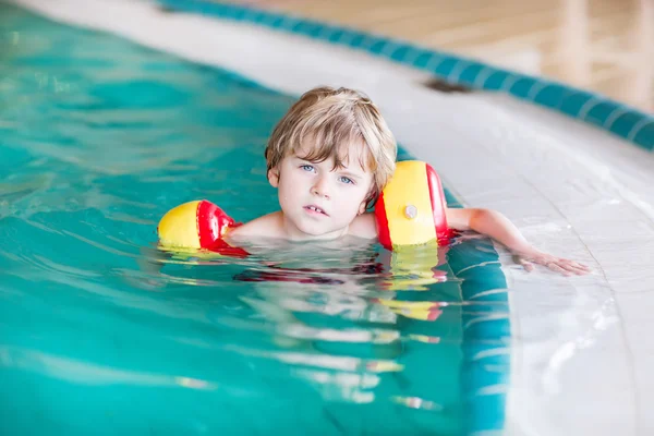 Pieni poika, jolla on uimareita opettelemassa uimaan uima-altaassa — kuvapankkivalokuva