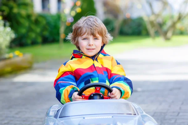 Маленький дошкольник за рулем большой игрушечной старинной машины, на открытом воздухе — стоковое фото