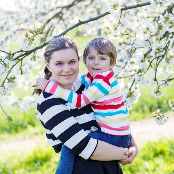Ung mamma och Lille unge pojken i blommande trädgård — Stockfoto