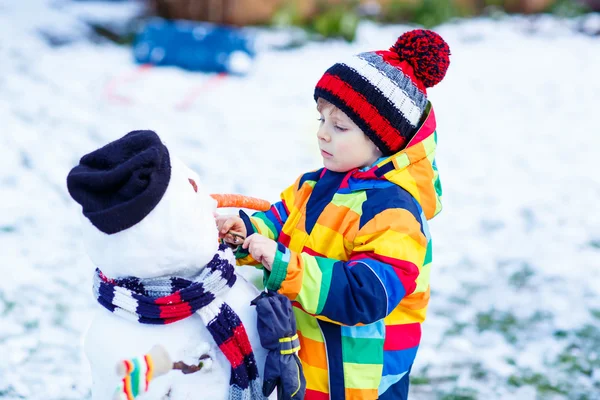 Funny kid boy making a snowman in winter — Stock Photo, Image