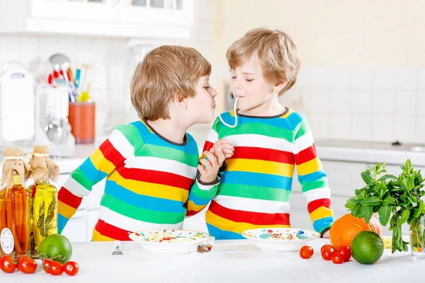 İki küçük çocuklar yerli mutfakta spagetti yiyen çocuk. — Stok fotoğraf