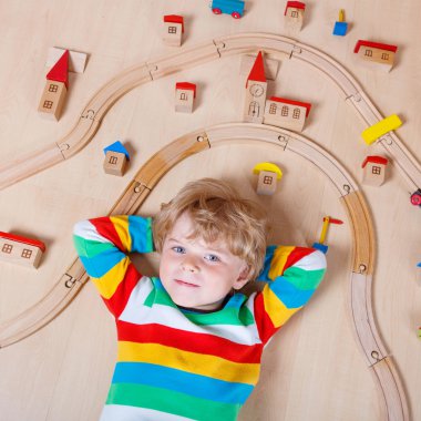 Little blond child playing with wooden railroad indoor