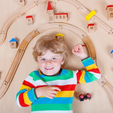 Little blond child playing with wooden railroad trains indoor