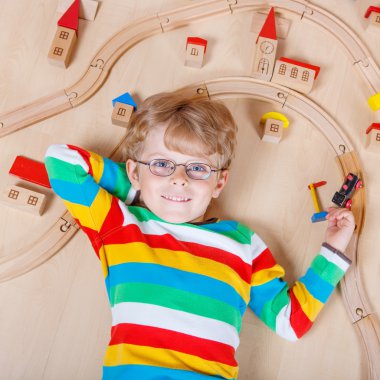 Little blond child playing with wooden railroad trains indoor