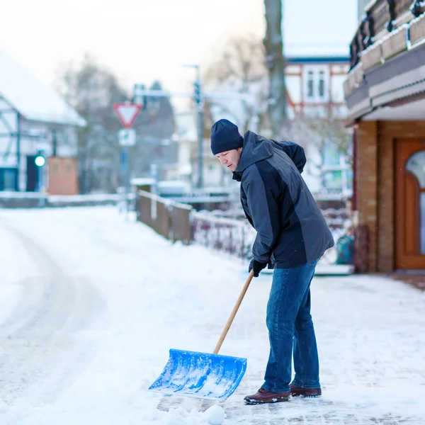 Чоловік зі сніжною лопатою чистить тротуари взимку — стокове фото