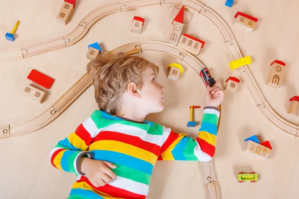 Pequena criança loira brincando com trens ferroviários de madeira interior — Fotografia de Stock