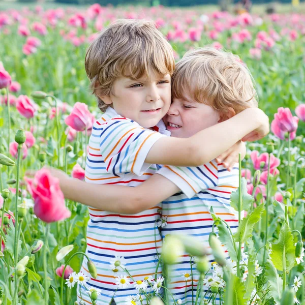 Twee gelukkige kleine blonde kinderen tijdens de bloei poppy veld — Stockfoto