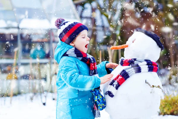 Funny kid boy i färgglada kläder att göra en snögubbe, utomhus — Stockfoto