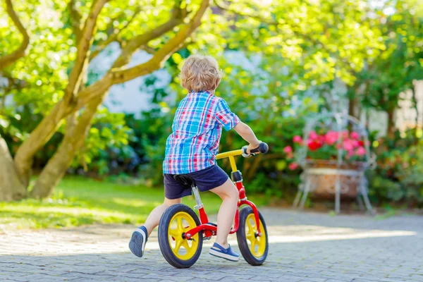 Мальчик водит трехколесный велосипед или велосипед в саду — стоковое фото