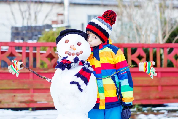 Funny kid boy making a snowman in winter — Stock Photo, Image