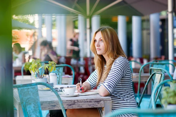 Женщина пьет кофе и пишет заметки в кафе — стоковое фото