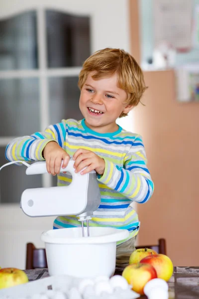 Funny blond kid boy baking apple cake indoors — Stock Photo, Image