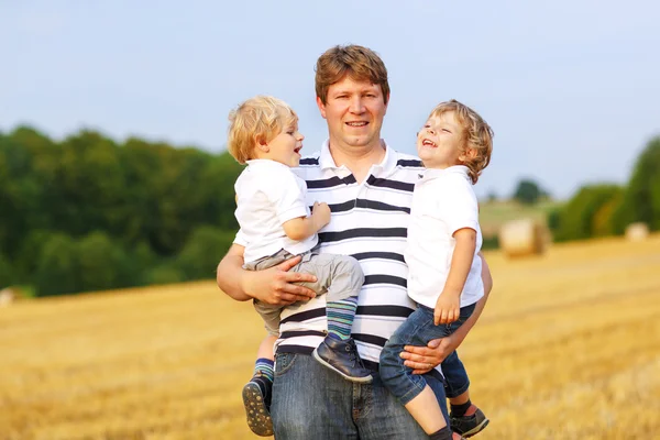 Jeune père et deux petits jumeaux garçons s'amuser sur le foin jaune — Photo