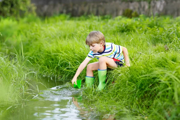 Lindo niño jugando con barcos de papel junto a un río —  Fotos de Stock