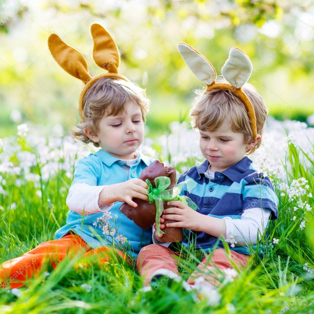 Two little kids playing with Easter chocolate bunny outdoors ⬇ Stock